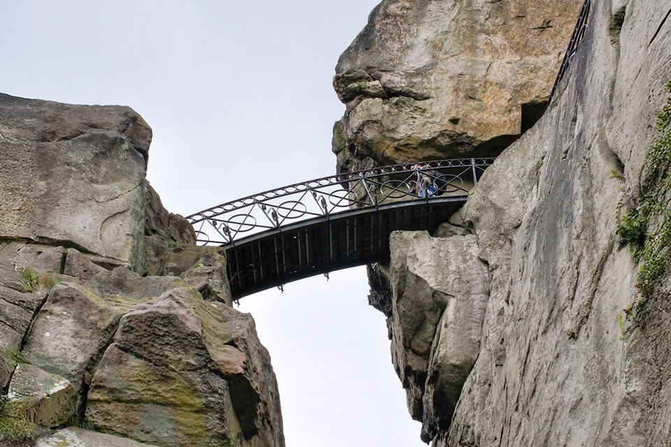 Eine Fußgängerbrücke aus Eisen verbindet zwei Felsen in luftiger Höhe.