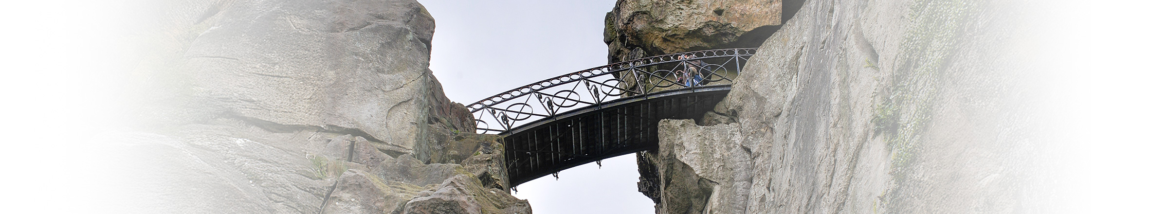 Eine Fußgängerbrücke aus Eisen verbindet zwei Felsen in luftiger Höhe.